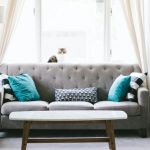 Bright living room with a grey sofa, decorative cushions, coffee table, and carpeted flooring, styled to reflect 5 Tiny secrets how to maintain a clean home of carpet flooring
